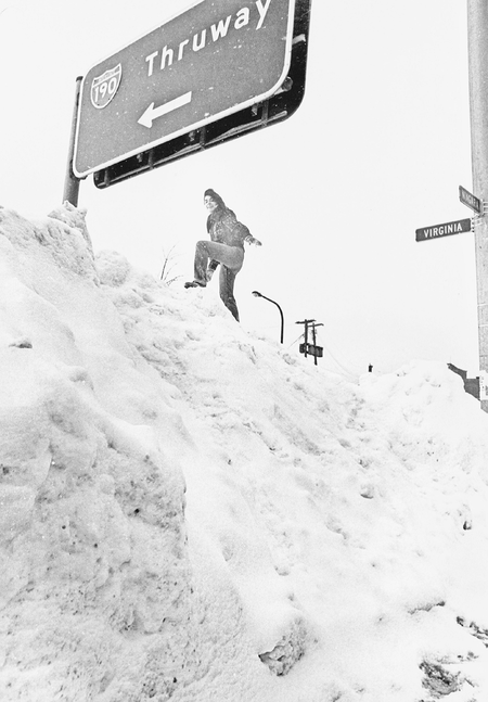 A young woman attempts to reach a highway sign during the Buffalo blizzard of 1977.